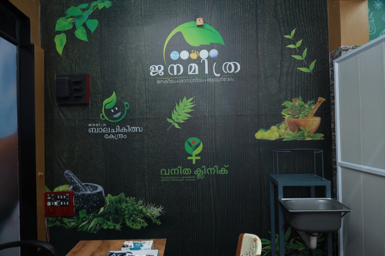 A consultation room at the centre, its wall carrying the Janamitra, Bala Chikitsa Kendram and Vanitha Clinic marks