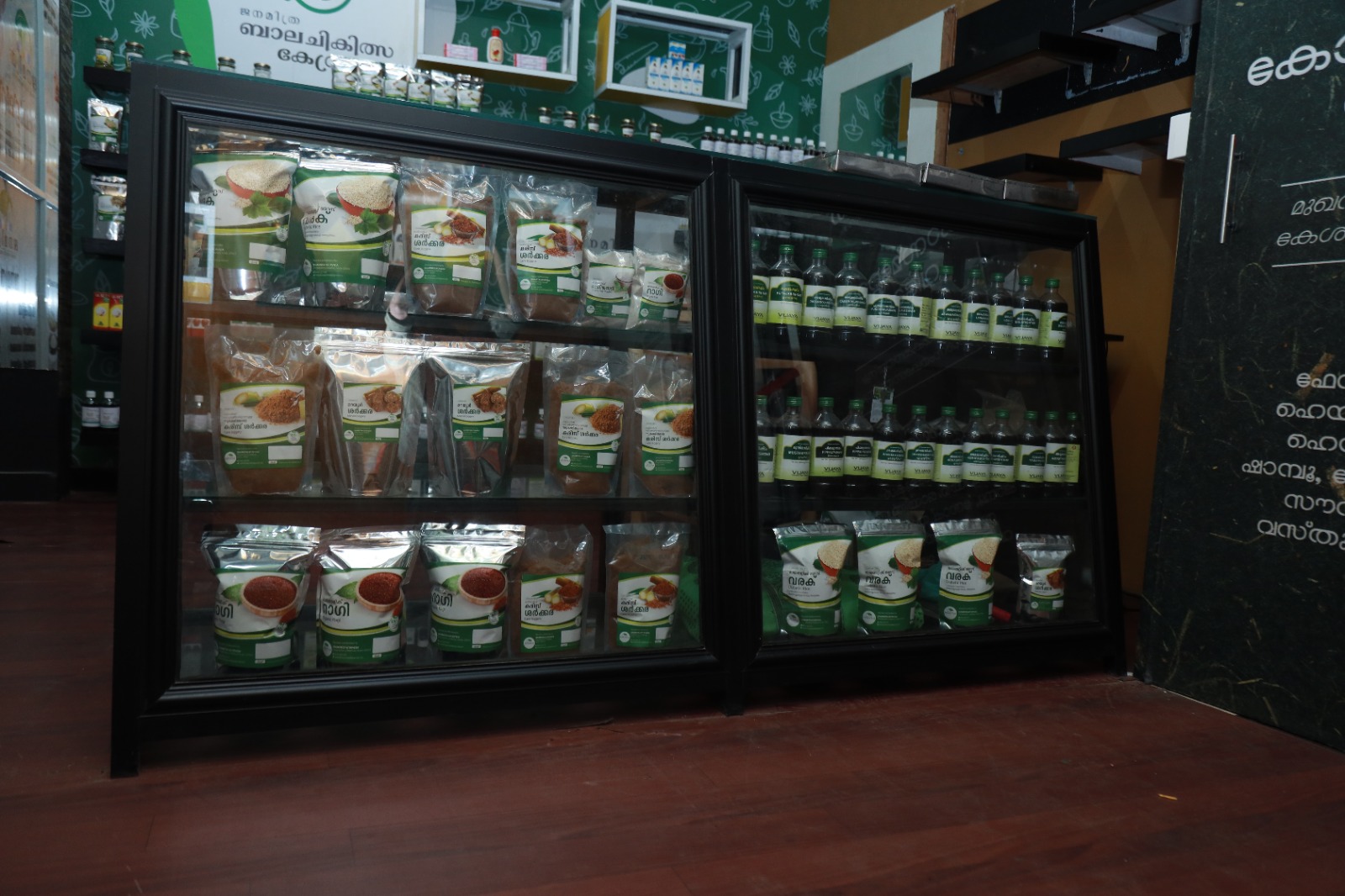Display cabinets of Janamitra products — jaggery, ragi and millet preparations alongside medicated oils
