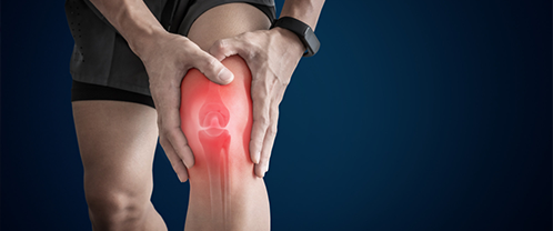 A person pausing on a staircase, resting a hand on a painful knee