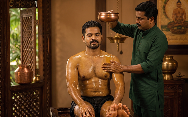 Warm medicated oil being squeezed from cloths over a patient